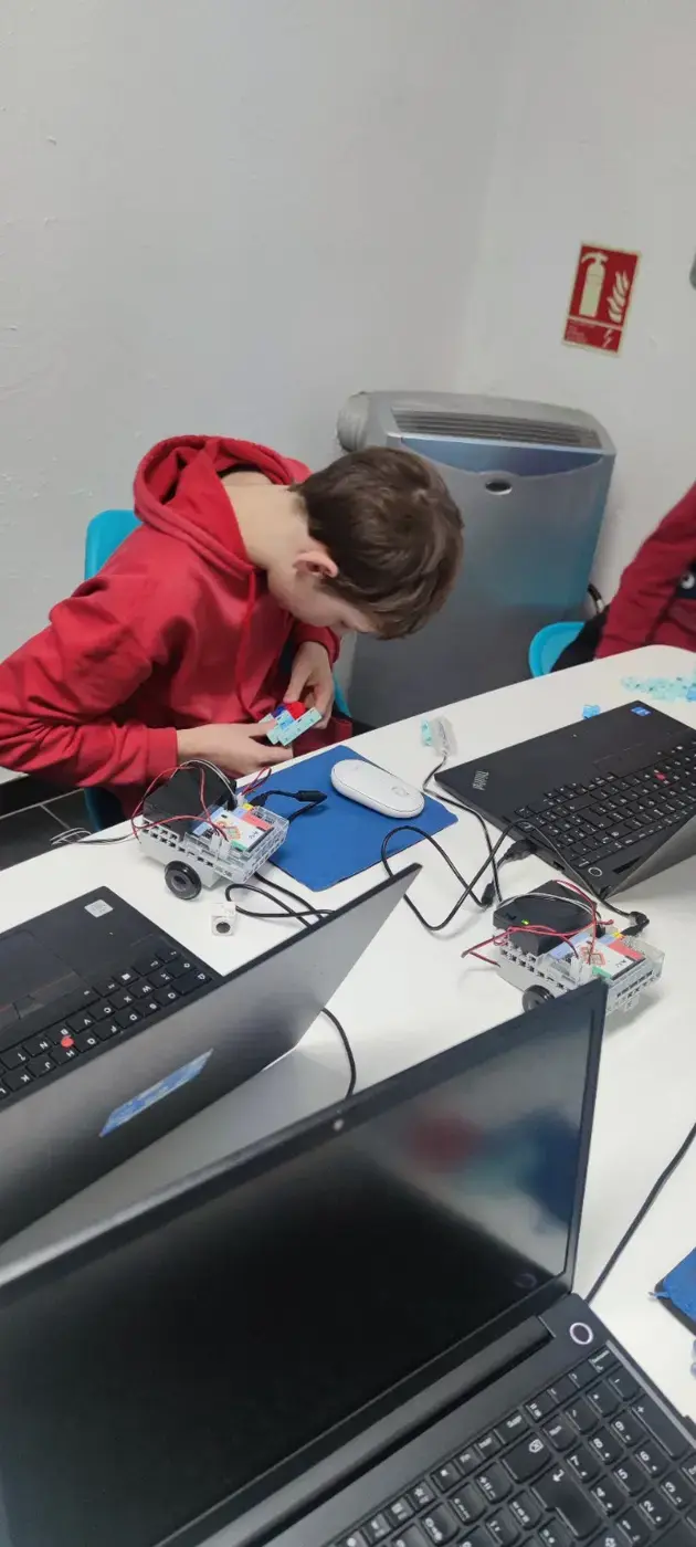 Un participant prépare et câble deux robots mobiles à côté de plusieurs ordinateurs.